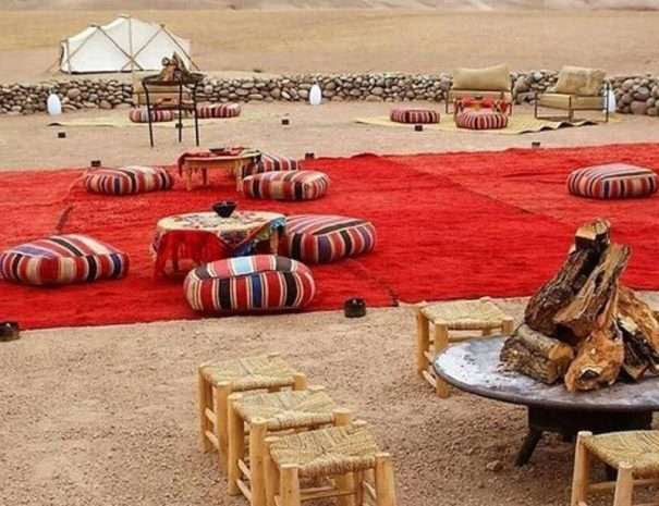 Nomad picnic setup in the Agafay desert with red Berber rugs, poufs and a fire pit