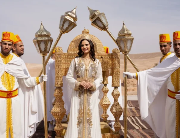 Bride in a traditional Moroccan takchita on a golden amaria throne with attendants during a wedding photoshoot in the Agafay Desert